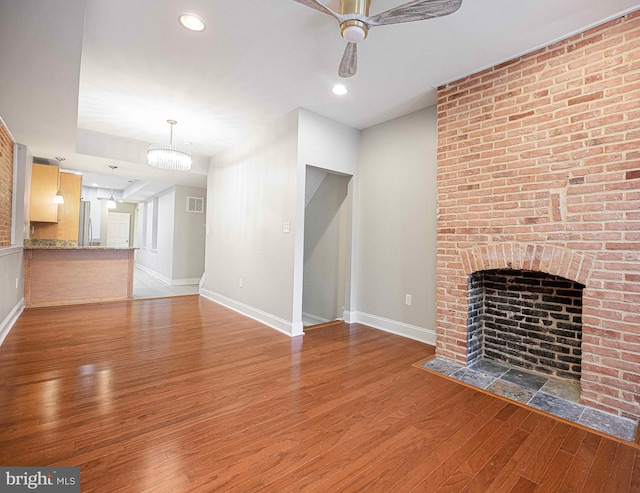 unfurnished living room featuring ceiling fan with notable chandelier, light hardwood / wood-style floors, and a fireplace