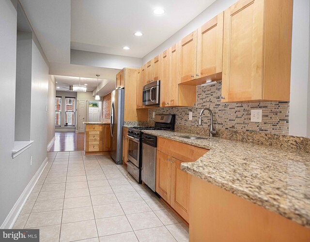 kitchen with tasteful backsplash, sink, hanging light fixtures, appliances with stainless steel finishes, and light stone countertops