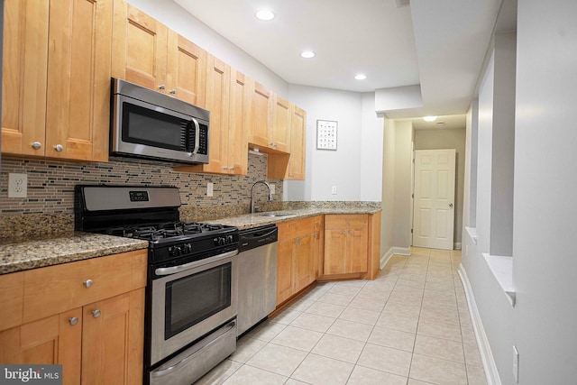 kitchen with light tile patterned floors, sink, tasteful backsplash, appliances with stainless steel finishes, and light stone countertops