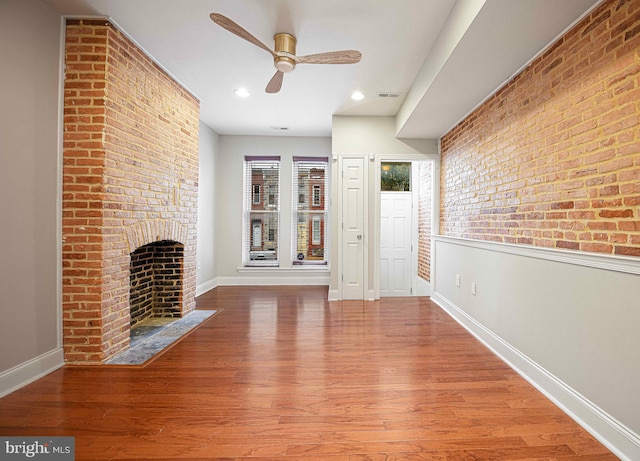 unfurnished living room with brick wall, hardwood / wood-style floors, ceiling fan, and a brick fireplace