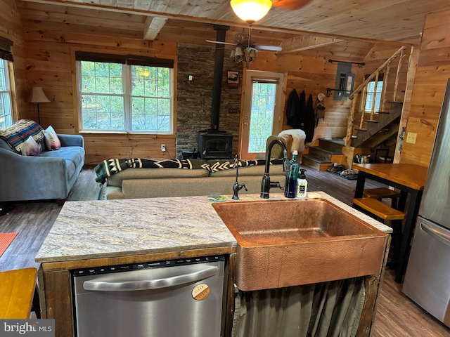 kitchen with a wood stove, stainless steel appliances, ceiling fan, a wealth of natural light, and hardwood / wood-style floors