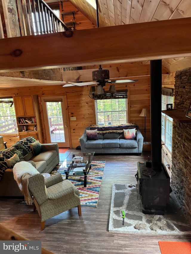 living room featuring ceiling fan, wood walls, a wood stove, hardwood / wood-style flooring, and lofted ceiling with beams