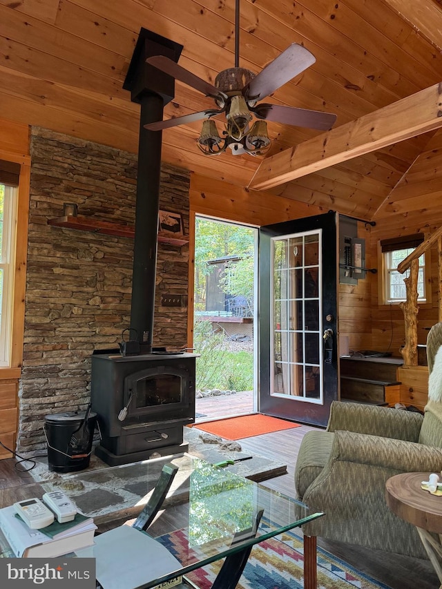 living room featuring wood ceiling, a wood stove, ceiling fan, vaulted ceiling with beams, and wooden walls