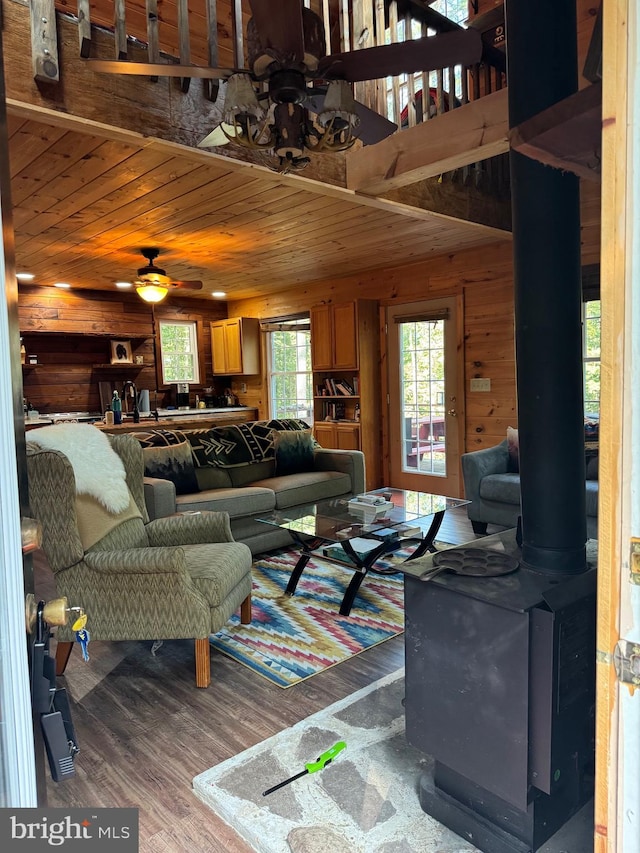 living room featuring wood ceiling, wood walls, a wood stove, ceiling fan, and hardwood / wood-style flooring