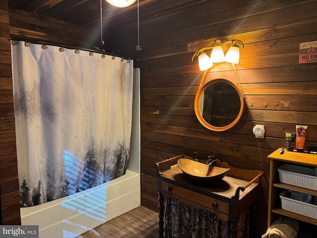 bathroom featuring wooden walls, wood-type flooring, vanity, and shower / tub combo with curtain