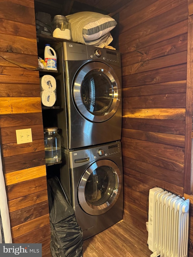 laundry area featuring radiator, wood walls, stacked washer / dryer, and dark hardwood / wood-style flooring