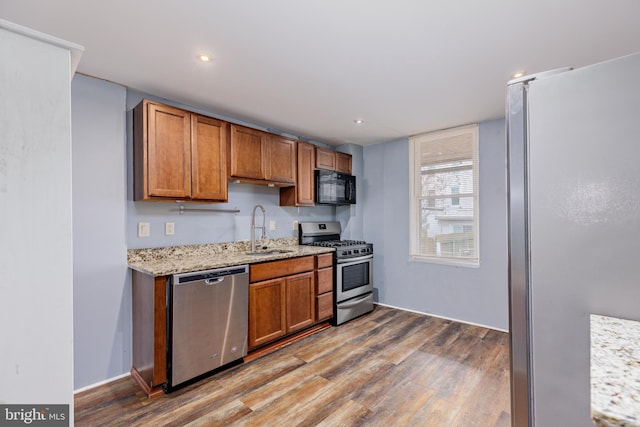 kitchen with hardwood / wood-style floors, light stone counters, sink, and appliances with stainless steel finishes