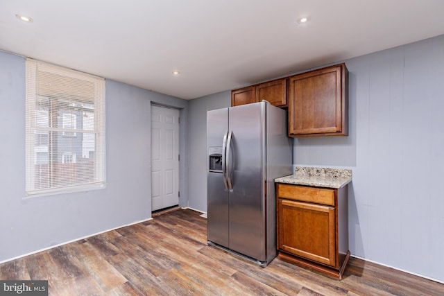 kitchen featuring light stone countertops, wood-type flooring, and stainless steel fridge with ice dispenser