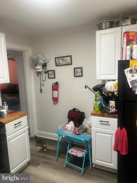 interior space with black fridge, hardwood / wood-style floors, wooden counters, and white cabinetry