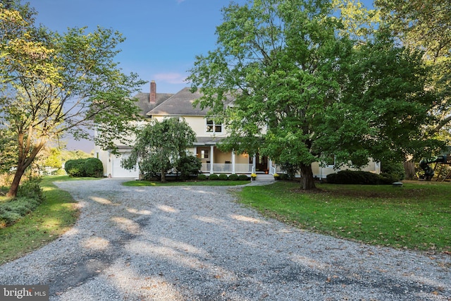 view of property hidden behind natural elements featuring a lawn, a porch, and a garage