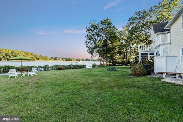 yard at dusk featuring a water view and a balcony