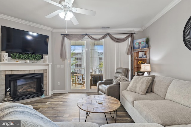 living room featuring a tiled fireplace, crown molding, ceiling fan, and hardwood / wood-style floors