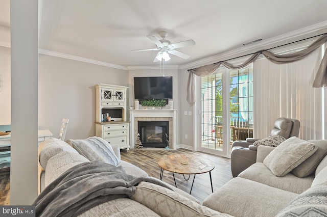 living room with ornamental molding, a tiled fireplace, light wood-type flooring, and ceiling fan