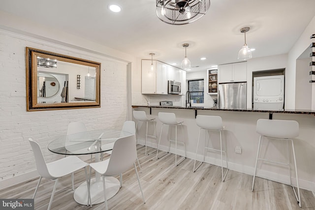 dining room with stacked washer / drying machine, light hardwood / wood-style floors, and brick wall