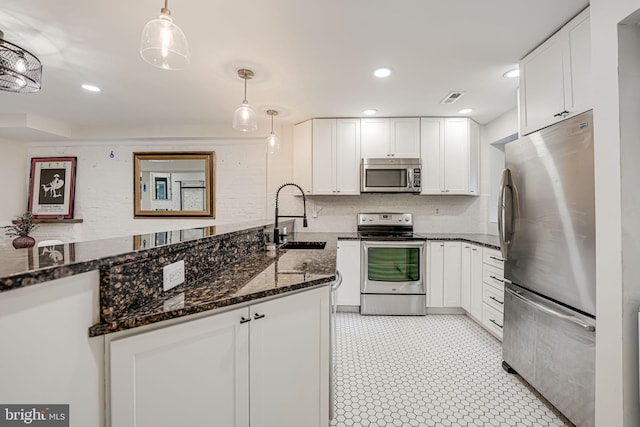 kitchen with white cabinetry, pendant lighting, stainless steel appliances, dark stone counters, and sink