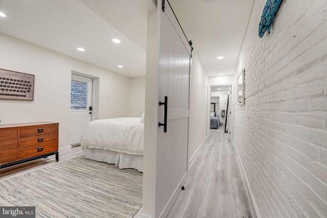 bedroom with a barn door, light wood-type flooring, and brick wall