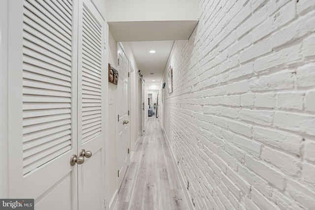 hallway with light hardwood / wood-style flooring and brick wall