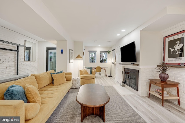 living room featuring a fireplace, light hardwood / wood-style flooring, and brick wall