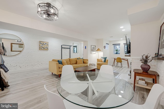 dining room with a chandelier, light hardwood / wood-style floors, and brick wall