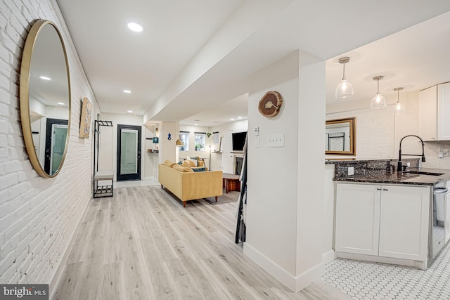 kitchen featuring pendant lighting, light hardwood / wood-style floors, sink, white cabinets, and dark stone countertops