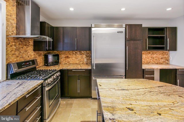 kitchen featuring wall chimney exhaust hood, light stone counters, appliances with stainless steel finishes, and tasteful backsplash