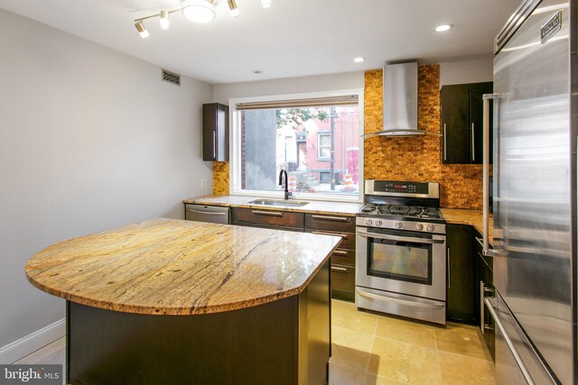 kitchen with sink, wall chimney range hood, a kitchen island, stainless steel appliances, and light stone countertops