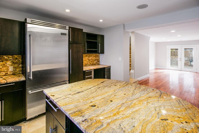 kitchen featuring stainless steel built in refrigerator, tasteful backsplash, a center island, light stone countertops, and light hardwood / wood-style floors