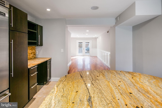 kitchen with light wood-type flooring, french doors, built in fridge, light stone countertops, and decorative backsplash