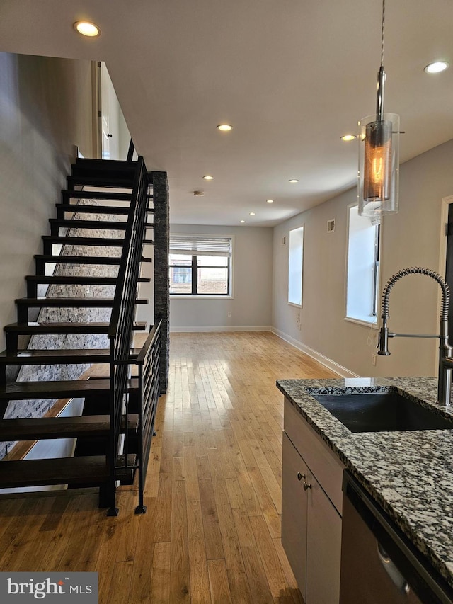 kitchen with light wood-type flooring, stone counters, decorative light fixtures, stainless steel dishwasher, and sink