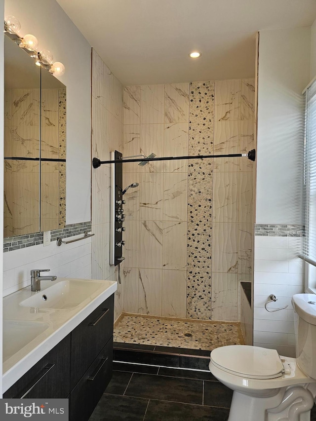 bathroom with tile walls, tiled shower, vanity, and toilet