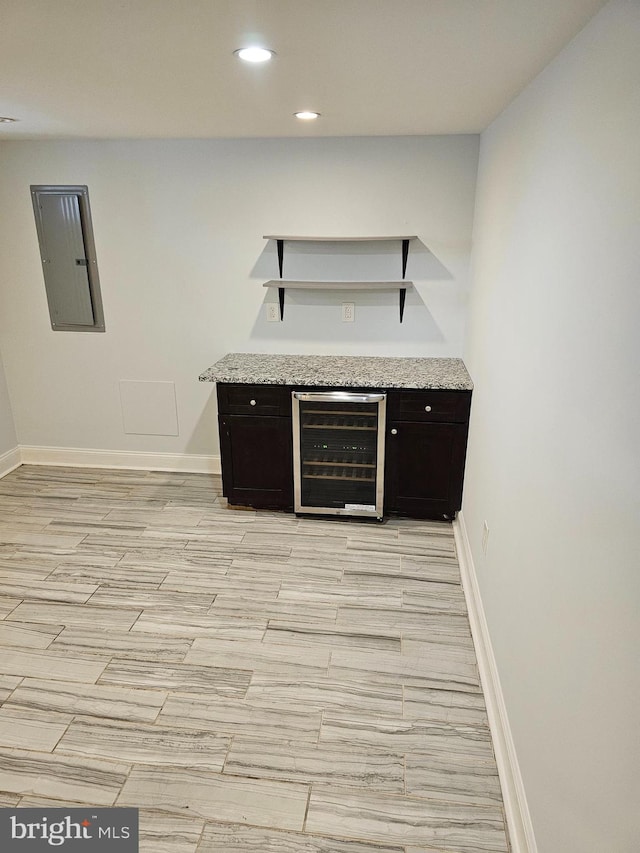 kitchen with dark brown cabinets, wine cooler, light stone counters, and electric panel