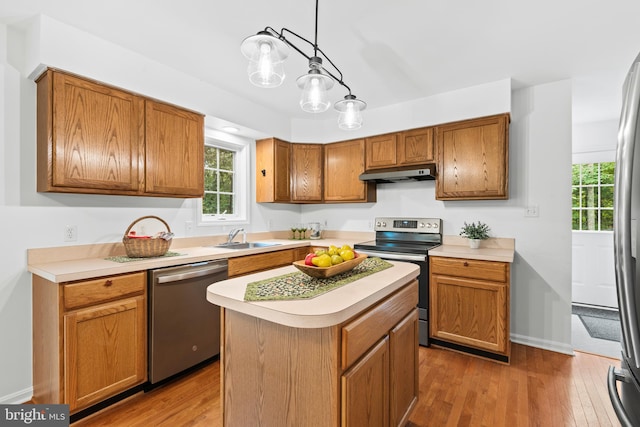 kitchen with hanging light fixtures, stainless steel appliances, a center island, hardwood / wood-style flooring, and sink