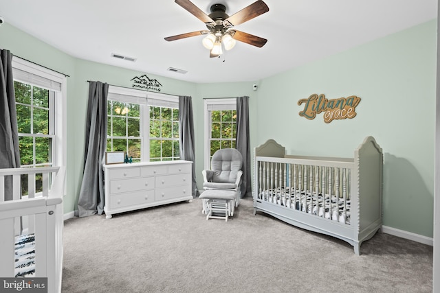 carpeted bedroom featuring a crib and ceiling fan