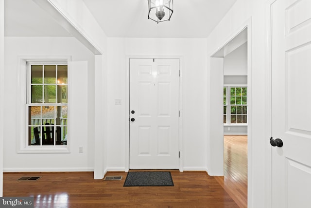 foyer entrance featuring a notable chandelier, a wealth of natural light, and dark wood-type flooring