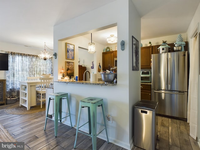 kitchen with hanging light fixtures, stainless steel refrigerator, dark hardwood / wood-style floors, and a breakfast bar