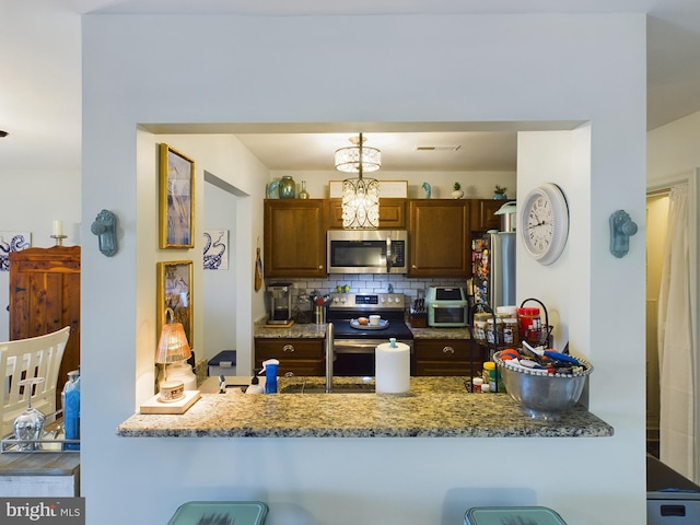 kitchen featuring pendant lighting, a breakfast bar area, stainless steel appliances, backsplash, and stone countertops