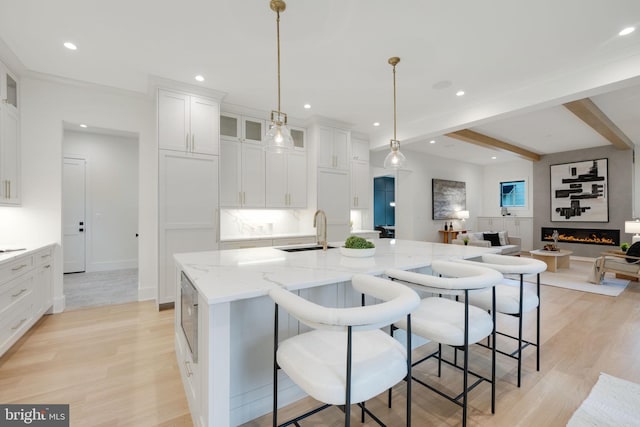 kitchen with an island with sink, white cabinets, a fireplace, pendant lighting, and sink