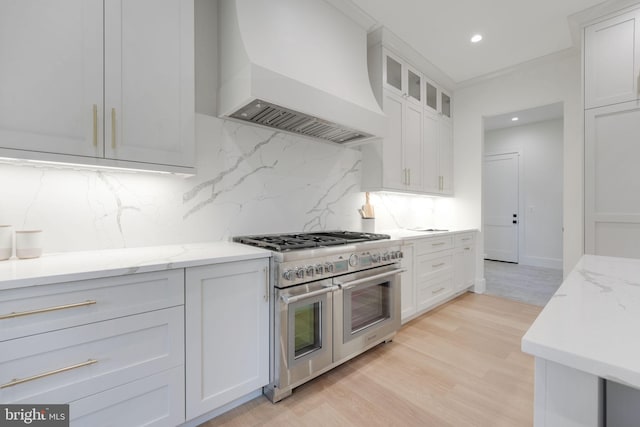 kitchen featuring white cabinetry, tasteful backsplash, range with two ovens, light wood-type flooring, and custom exhaust hood