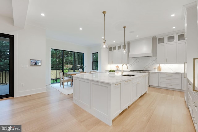 kitchen featuring white cabinets, premium range hood, sink, a kitchen island with sink, and light hardwood / wood-style floors