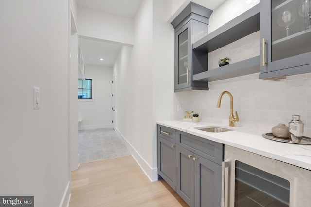 bar featuring light stone countertops, light hardwood / wood-style floors, sink, and beverage cooler