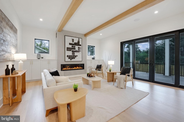 living room with light hardwood / wood-style flooring, a large fireplace, beamed ceiling, and plenty of natural light