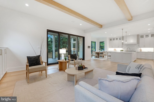 living room featuring light wood-type flooring, sink, and beamed ceiling