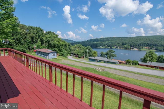 wooden terrace featuring a storage shed, a water view, and a yard