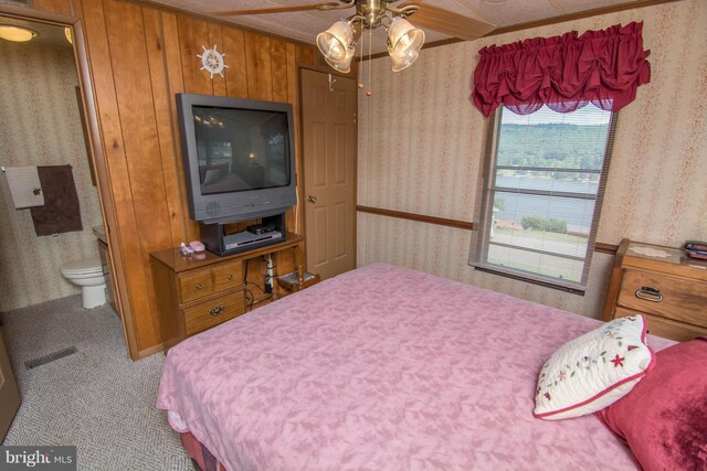 carpeted bedroom featuring ceiling fan, wooden walls, crown molding, and ensuite bathroom