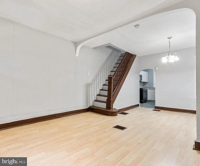 unfurnished living room with an inviting chandelier and light wood-type flooring