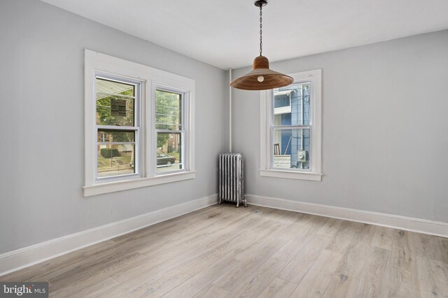 unfurnished room featuring light wood-type flooring, radiator heating unit, and plenty of natural light