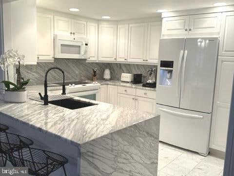 kitchen featuring white cabinetry, tasteful backsplash, refrigerator with ice dispenser, kitchen peninsula, and sink