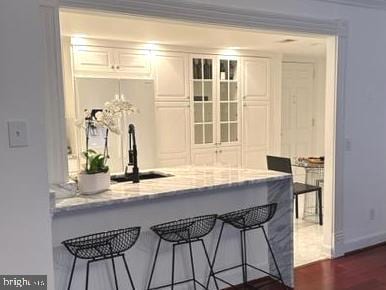 bar with light stone countertops, white cabinetry, and dark wood-type flooring