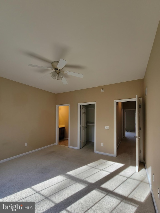 unfurnished bedroom featuring connected bathroom, ceiling fan, a walk in closet, light carpet, and a closet