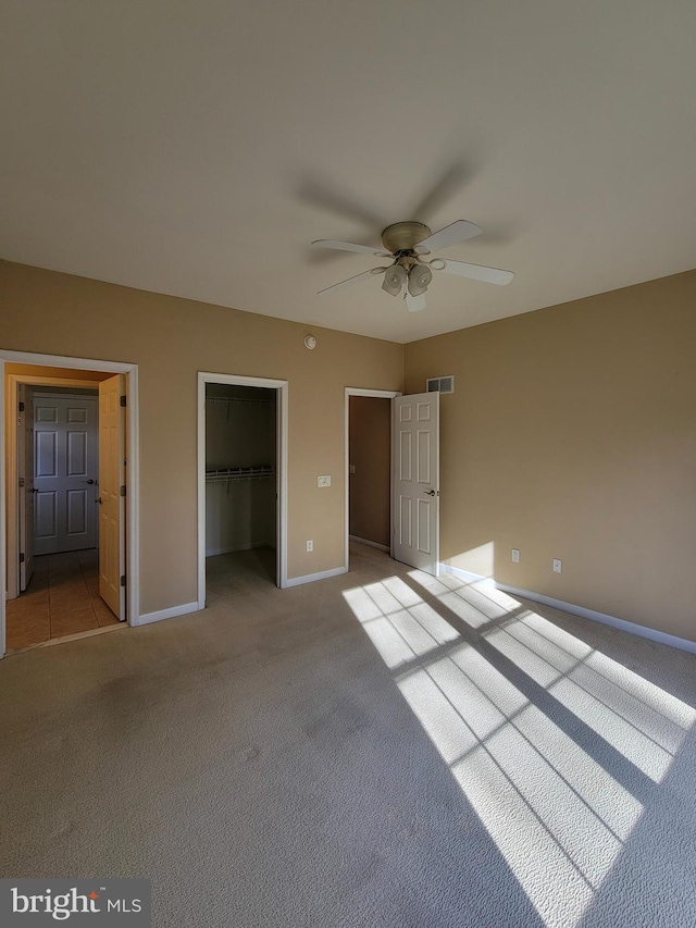 unfurnished bedroom featuring a walk in closet, ceiling fan, a closet, and light colored carpet